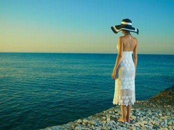 Elegant young woman in a hat standing on beach