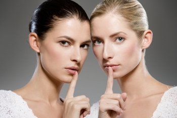 two young caucasian women gesturing shh - keep it secret
