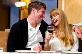 laughing embracing couple is sitting at restaurant and drinking wine