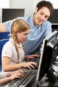 Teacher helping girl using computer in class