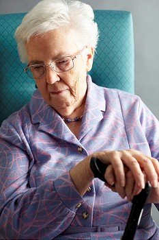 Unhappy Senior Woman Sitting In Chair Holding Walking Stick