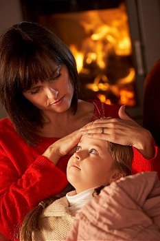 Mother Comforting Sick Daughter On Sofa By Cosy Log Fire