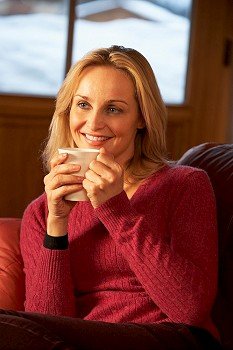 Middle Aged Woman Relaxing With Hot Drink On Sofa Watching TV