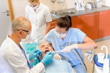 Dentist with nurses doing operation on senior male patient