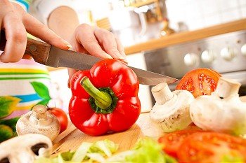 Woman´s hands cutting tomato bell pepper, behind fresh vegetables.
