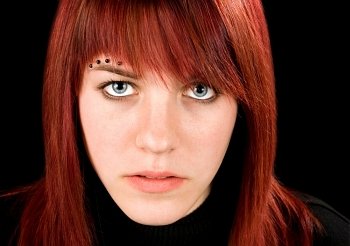 Simple frontal shot of a beautiful pierced redhead girl staring at the camera.  Studio shot.