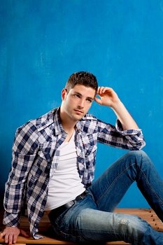 handsome young man with plaid shirt sitting on wood in blue background