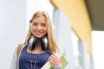 Student girl with headphones smiling at camera outdoor school building