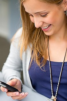 Smiling teenage woman reading text message on cellphone