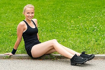 Happy young woman resting after outdoor workout sitting on grass