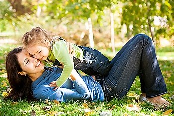 Full length portrait of woman with child lying on fall leaves in autumn park