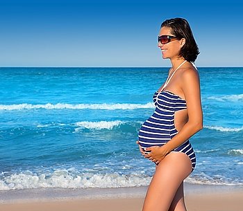 Beautiful pregnant woman walking on blue beach in summer vacation