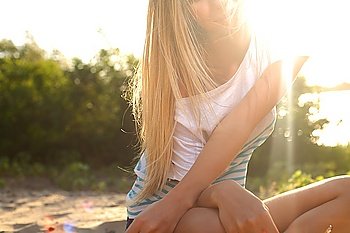 blond girl sitting near river against sun
