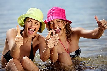 Two female friends at the beach giving thumbs-up
