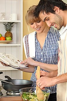 Woman and man smiling cooking using cookbook