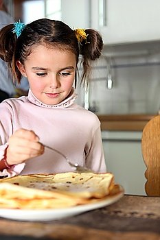 Little girl eating pancakes in kitchen