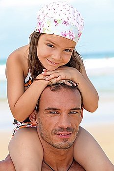 little girl sitting on father´s shoulders on the beach