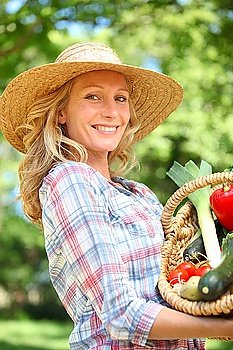 Woman smiling with a straw hat holding basket of vegetables.