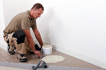 Carpet fitter applying adhesive over an old tiled floor