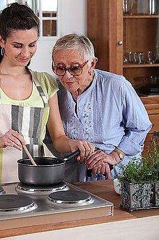 Young woman cooking for an elderly lady