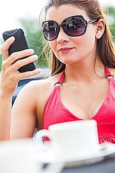 A beautiful young woman texting on her mobile cell phone while drinking coffee in a cafe