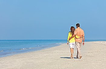 Rear view of man and woman romantic couple in white clothes walking on a deserted tropical beach with bright clear blue sky