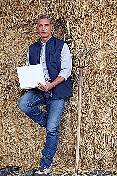 a farmer with a computer leaning against straw bales