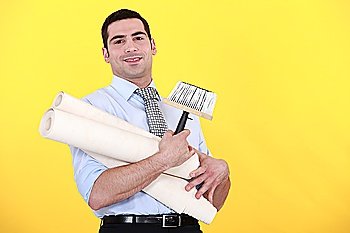young handsome man carrying rolls of wallpaper against yellow background