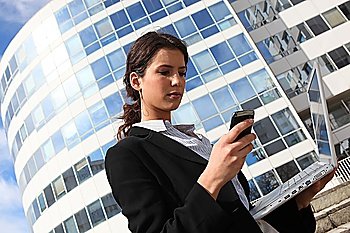 Brunette businesswoman stood outdoors with laptop and mobile