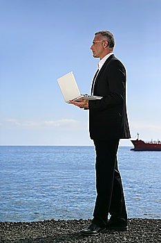 Businessman stood holding a laptop at the beach