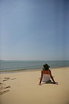 Woman sat on a beach looking out at sea