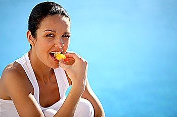 Woman kneeling by swimming pool eating fruit