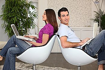 Couple using laptops in matching chairs