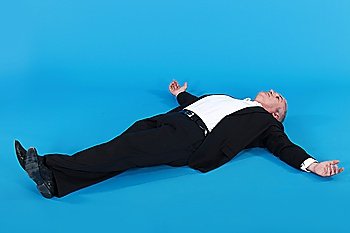 mature man in suit lying on his back with arms wide apart against blue background