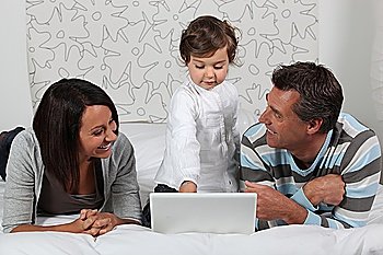 Parents and daughter in bed with laptop