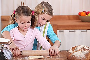 Sisters using rolling pin to roll dough