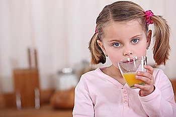 A little girl drinking orange juice in the kitchen.