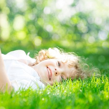 Happy child lying on green grass outdoors in spring park