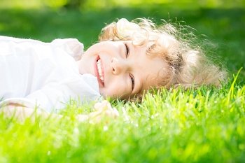 Happy child lying on green grass in spring park