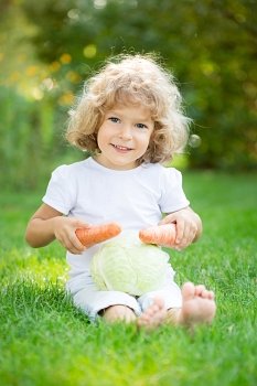Happy child playing with vegetables on green grass outdoors in spring park