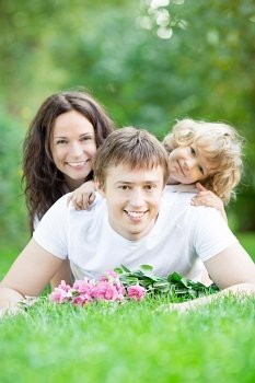 Happy family lying on grass in spring park against blurred green background