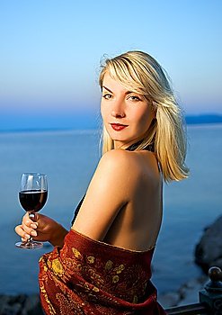 Beautiful young woman drinks red wine near the ocean