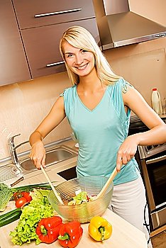Beautiful young woman mixing vegetable salad in a glass bowl
