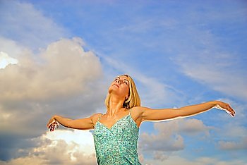 Beautiful blond girl with arms wide open over blue cloudy sky