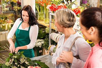 Young florist preparing cut flowers shop buyers bouquet customers