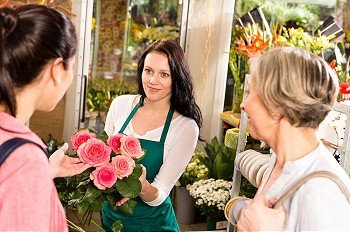 Happy young florist woman showing roses flowers customers shop