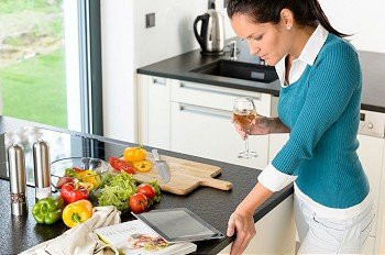 Young woman reading tablet recipe kitchen preparing food looking wine