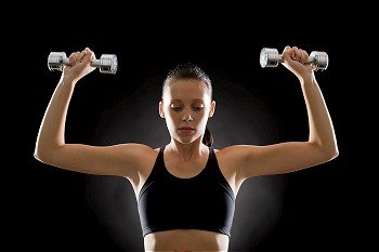 Portrait of sporty young woman holding dumbbells on black background