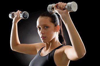 Portrait of sporty young woman holding dumbbells on black background