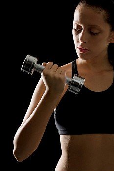 Portrait of sporty young woman holding dumbbell on black background
